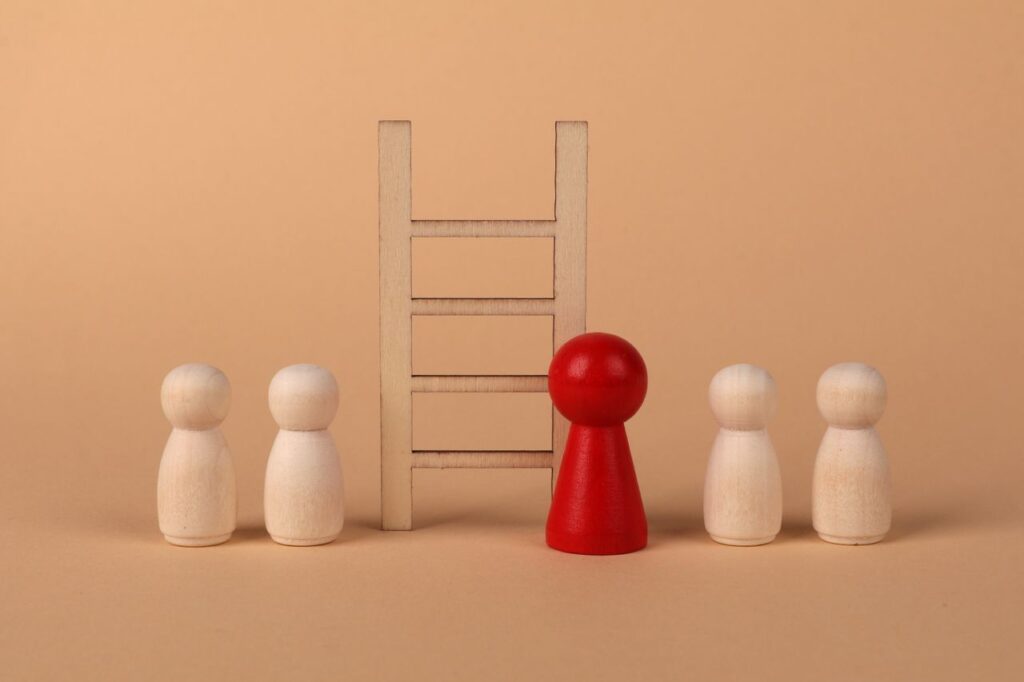 Abstract representation of leadership with wooden figures and ladder on a neutral background.